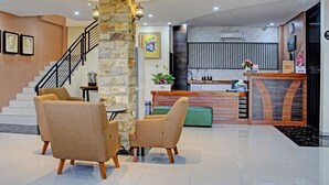 A lobby with a reception desk, a staircase, and seating area. - Capital O 92583 Raja Soeta Hostel Syariah (Bandar Lampung)