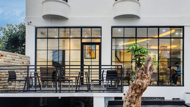 A modern building with large windows, outdoor seating, and a tree in the foreground. - Capital O 92583 Raja Soeta Hostel Syariah (Bandar Lampung)