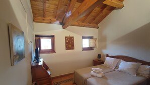 A bedroom with a wooden ceiling, two beds, a desk, a chair, and a small window. - Posada Restaurante de Serrada (Puentes Viejas)