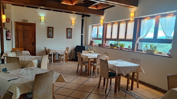 A dining area with multiple tables and chairs, wooden beams on the ceiling, and potted plants by the windows. - Posada Restaurante de Serrada (Puentes Viejas)