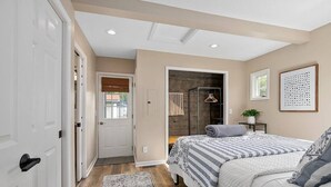 Une chambre à coucher avec un lit, une table de chevet, une lampe suspendue, une porte et une fenêtre.