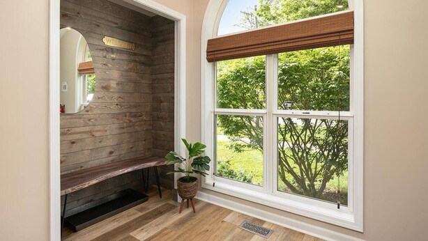 Une pièce avec un banc en bois, une grande fenêtre en arc de cercle dotée de stores et une plante en pot.