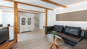 A modern living room with a wooden ceiling, a black leather sofa, a glass coffee table, and a TV on a wooden stand. - Holiday home in the middle of the old town of Goslar for up to 6 people (Goslar)