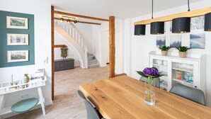 A dining area with a wooden table, chairs, and a vase with a flower. There is a staircase in the background and a shelf with decorative items. - Holiday home in the middle of the old town of Goslar for up to 6 people (Goslar)