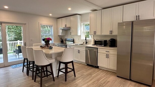 Una cocina moderna con armarios blancos, electrodomésticos de acero inoxidable y una isla central con taburetes de bar.