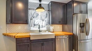 A kitchen with dark cabinets, a stainless steel refrigerator, a wooden countertop, and a window with a floral curtain. - Charming Retreat in Charlottesville w/ Deck! (Charlottesville)