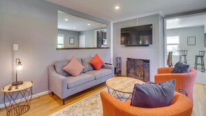 A modern living room with a grey sofa, orange armchairs, a round coffee table, and a fireplace. - Charming Retreat in Charlottesville w/ Deck! (Charlottesville)