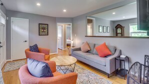 A modern living room with a grey sofa, orange armchairs, a round coffee table, and a black baby gate. - Charming Retreat in Charlottesville w/ Deck! (Charlottesville)