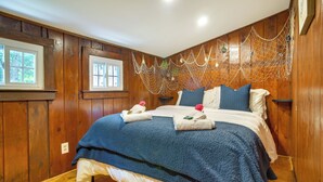 Een kamer met houten lambrisering, een bed, twee ramen en een decoratief net boven het bed.