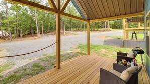 Un espacio exterior cubierto con terraza de madera, muebles de mimbre y vistas a un área boscosa.