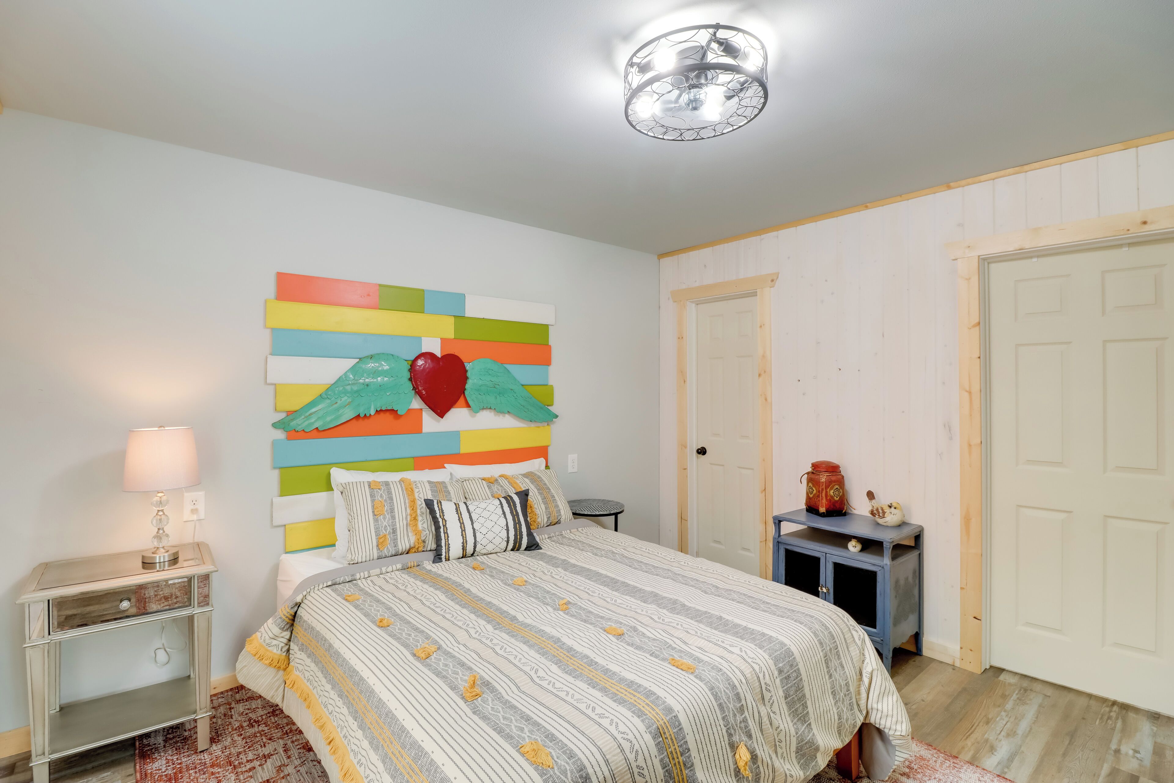 Une chambre à coucher avec un lit, une table de chevet, une lampe et un élément de décoration murale aux couleurs vives.