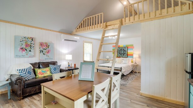 Ett mysigt rum med en säng på ett loft, en trästege, ett matbord och en soffa.