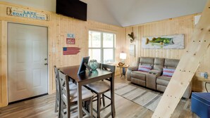 Een blokhutinterieur met een eettafel, een bank en een aan de muur bevestigde televisie.