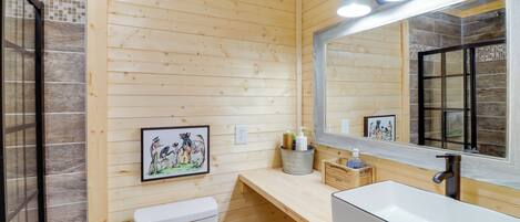 A wooden-paneled bathroom with a white sink, a toilet, and a mirror. There are two wall-mounted lights above the mirror and a framed picture on the wall.