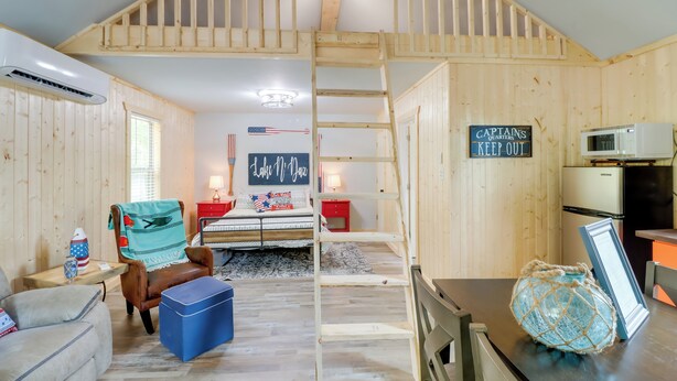 Interieur van een blokhut met een slaapzolder, een kitchenette, een eethoek en een woonkamer met een bank en een fauteuil.