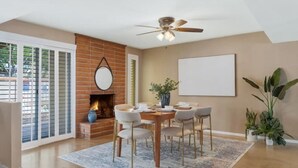 A dining area with a brick fireplace, a ceiling fan, and a large window with blinds. - Pool Fire Pit  Ping-Pong (Tucson)