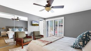 A bedroom with a bed, two chairs, a ceiling fan, a large mirror, and a window with blinds. - Pool Fire Pit  Ping-Pong (Tucson)