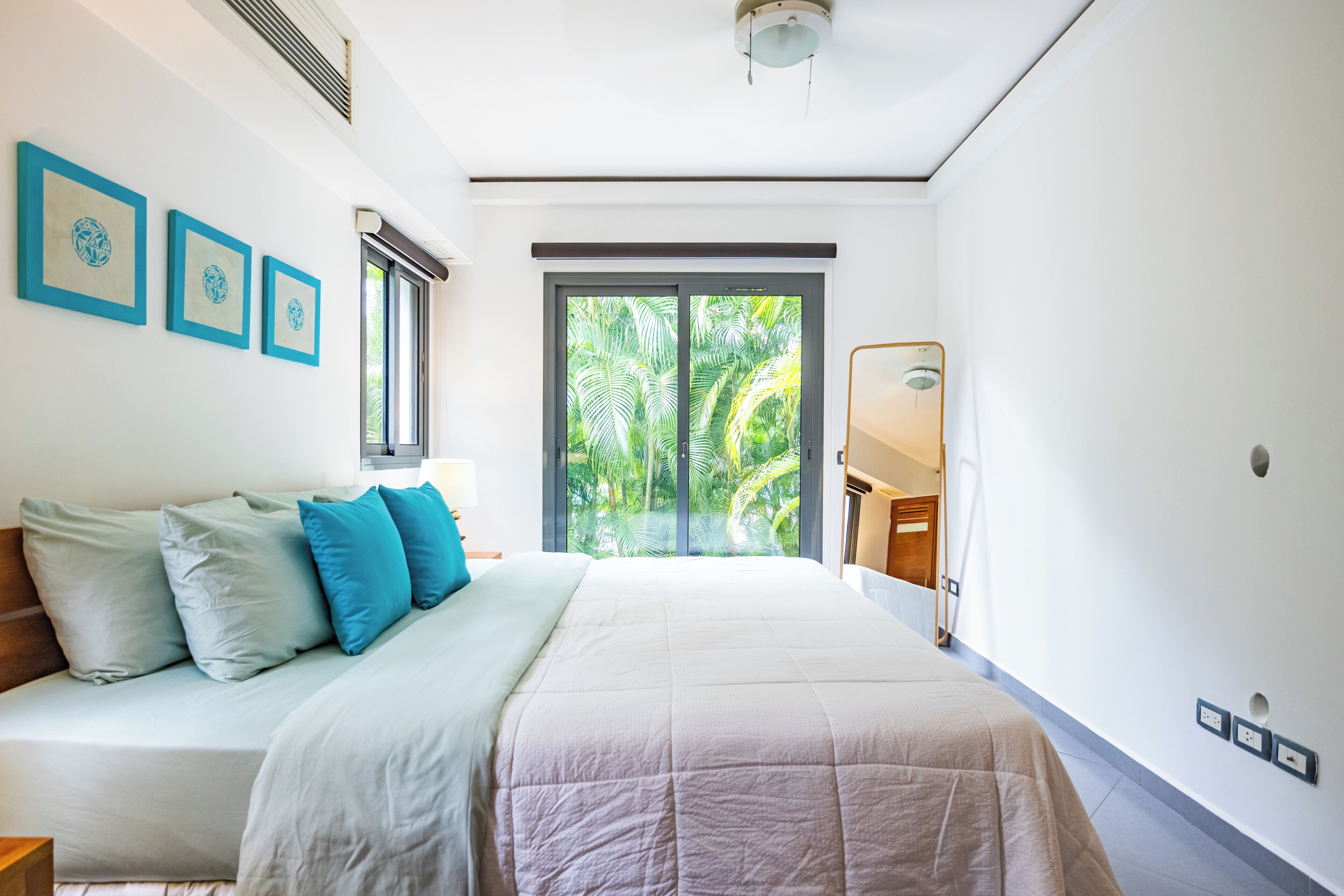 A modern bedroom with a large bed, a view of lush greenery through a sliding door, and a minimalist decor.