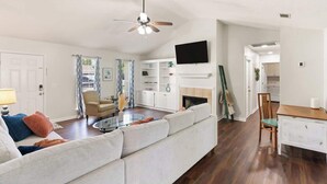 A modern living room with a sofa, a coffee table, a TV mounted on the wall, and a fireplace. - Once Upon a Tide/2 King Beds/Centrally Located (Brunswick)