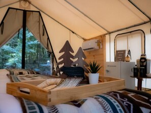 A tent interior with a bed, a tray table, a potted plant, and a coffee maker.