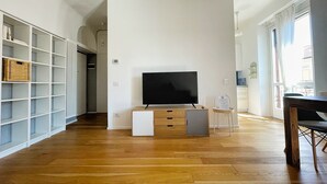 Een moderne woonkamer met een flatscreen televisie op een houten kast, een wit dressoir en een eethoek met een houten tafel en stoelen.