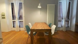 Een eetgedeelte met een houten tafel en stoelen, een hanglamp en ramen voorzien van zonwering.