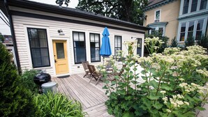 Une maison avec une terrasse en bois, une porte jaune et un parasol bleu.