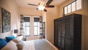 Une chambre à coucher avec un lit, un ventilateur de plafond, une fenêtre avec des rideaux et une armoire.