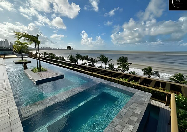 Una piscina con vistas a la playa y al océano, rodeada de palmeras y una terraza de madera.