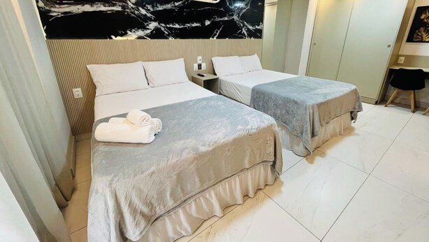 Habitació d'hotel amb dos llits, una paret de marbre i una petita taula amb una cadira.
