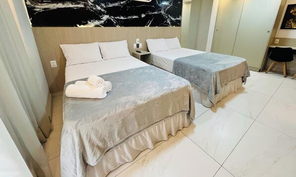 A hotel room with two beds, a marble wall, and a small desk with a chair. - LM UNITY CABO BRANCO (João Pessoa)
