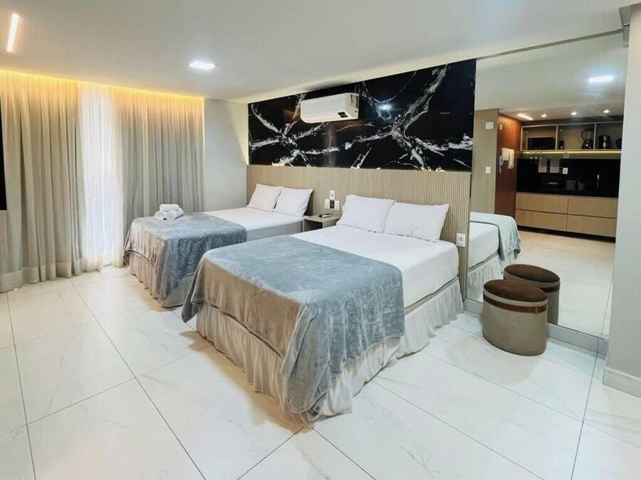 Habitación de hotel con dos camas, un espejo grande, kitchenette y baño con cortina.