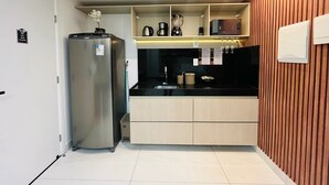 Une cuisine compacte comprenant un réfrigérateur, un plan de travail avec un évier et un mur d’accent en bois.
