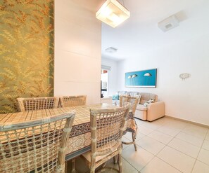 A dining area with a round table and chairs, a sofa, and a wall with a painting. - Residencial Ébano Marfim e Jequitibá (Ubatuba)