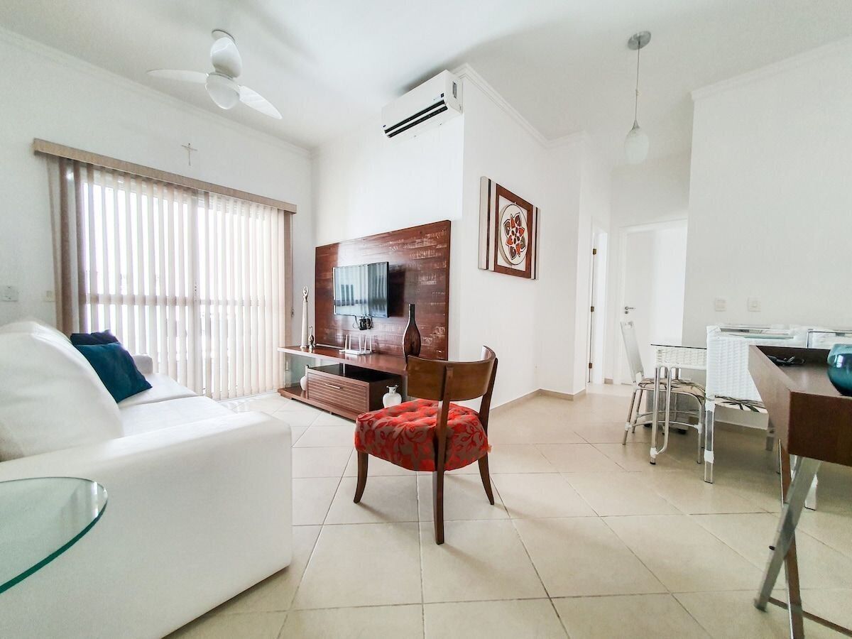 Una sala de estar moderna con un sofá blanco, una butaca tapizada en rojo, una zona de comedor con mesa y sillas, y una cocina con estufa y fregadero.