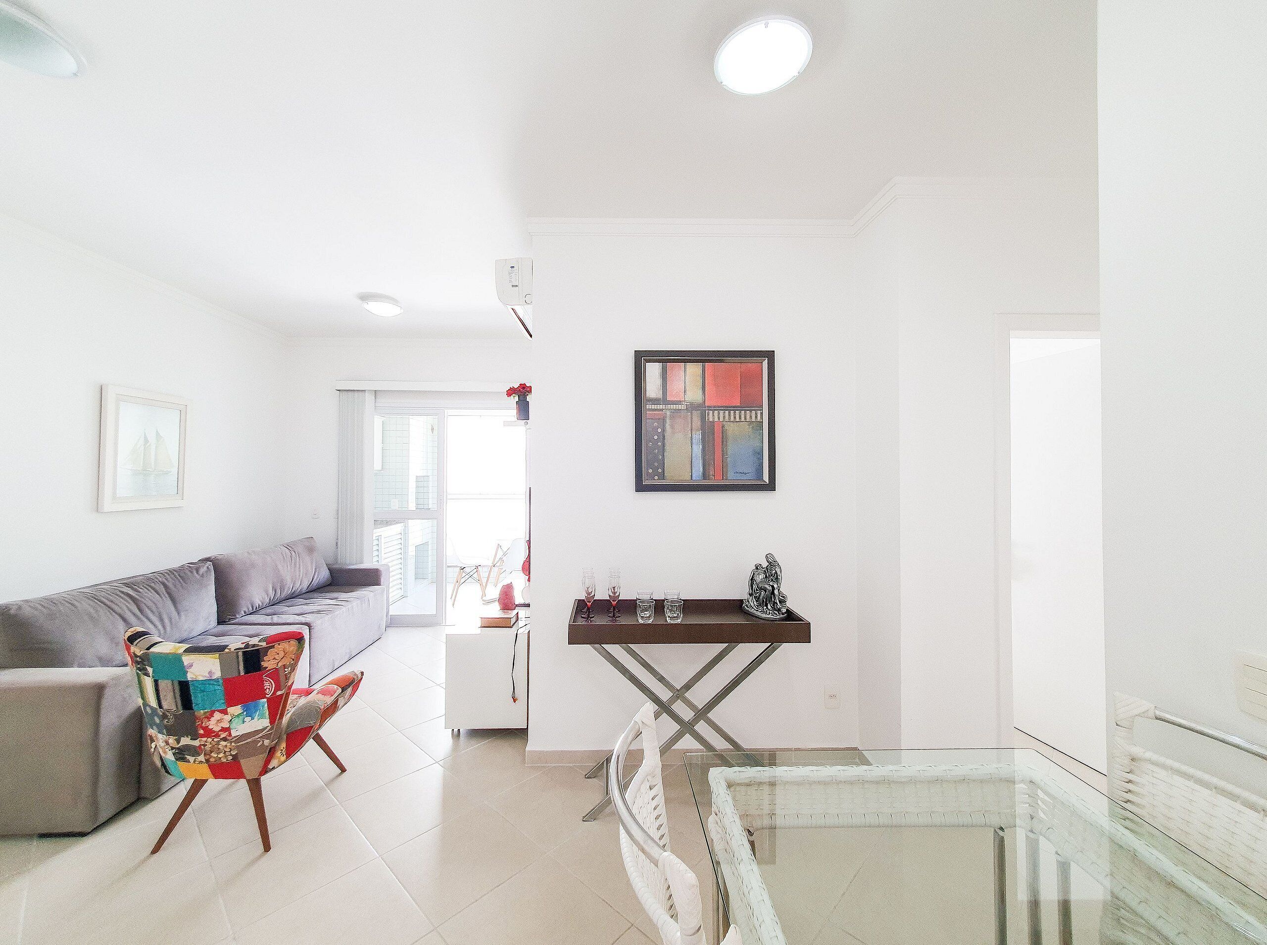 A modern living room with a grey sofa, a colorful chair, a glass table, and a framed abstract painting.