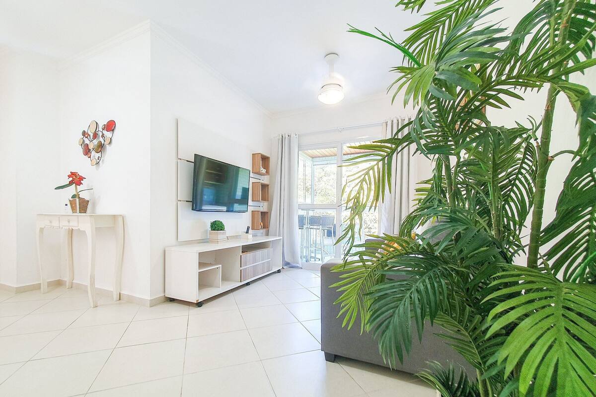 Un salon moderne avec un téléviseur à écran plat, une console blanche et une grande plante en pot.