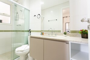 A modern bathroom with a glass-enclosed shower, a toilet, a sink with a mirror, and a small potted plant.