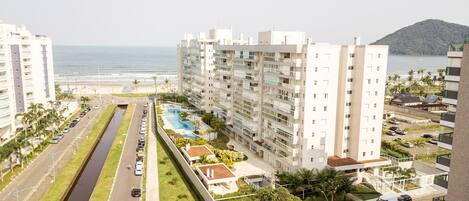 A high-rise hotel with a swimming pool, a road with parked cars, and a beach in the background.