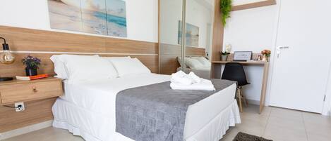 A modern hotel room with a large bed, a desk, and a mirror.