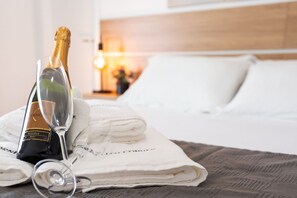 A bed with white linens and a folded towel, a bottle of champagne, and a wine glass on the bed.