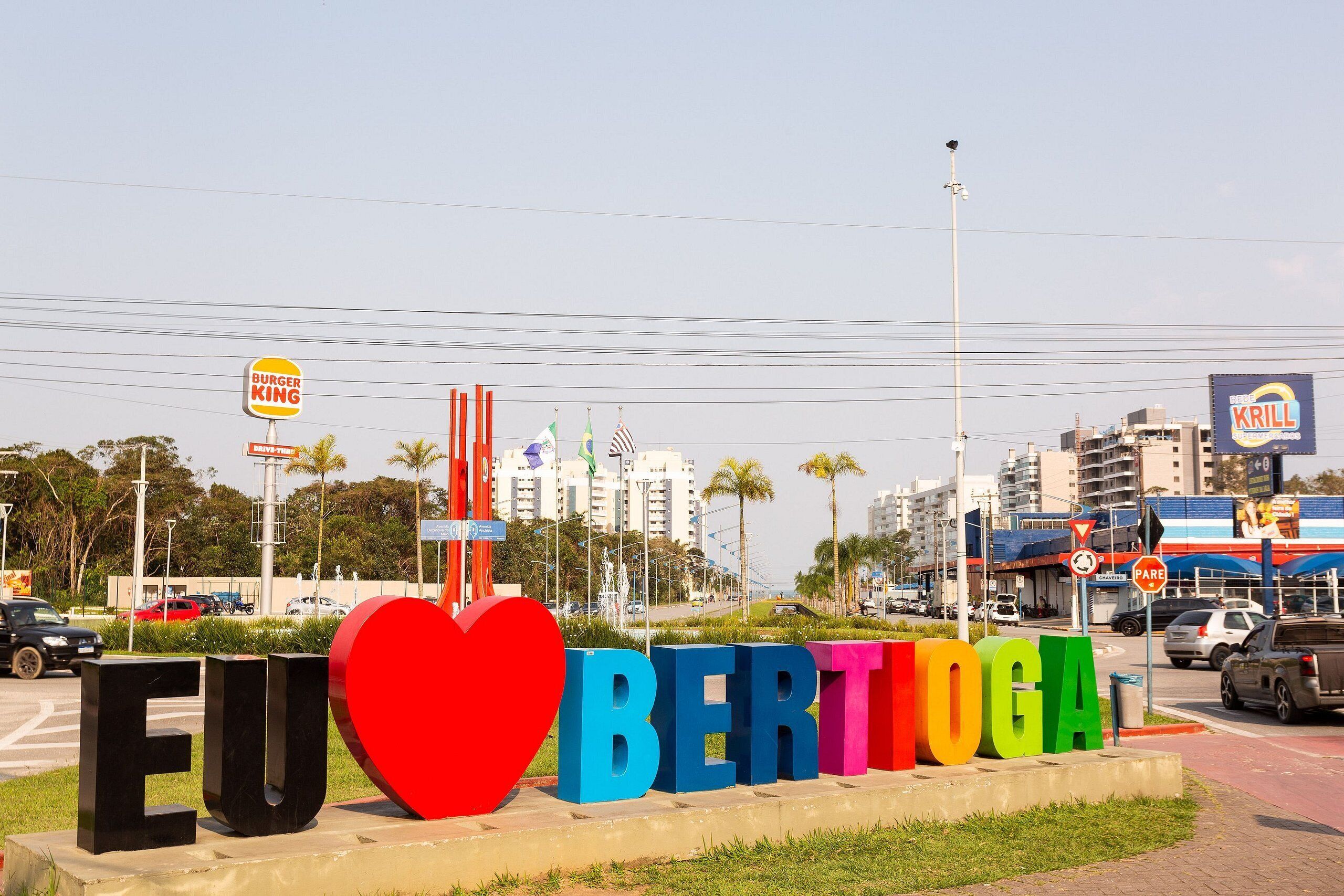 Um letreiro com a inscrição 'EUROBERTO' e um símbolo de coração, rodeado por vegetação e edifícios urbanos.
