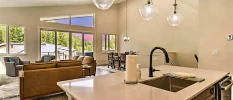 Una cocina moderna con una isla central, una zona de comedor con sofá y ventanas amplias que ofrecen vistas al exterior.