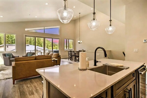 A modern kitchen with a central island, a dining area with a sofa, and large windows offering a view of the outdoors. - Opening Day Ski • Hot Tub • Pool Table • Sleeps 8 (Durango)