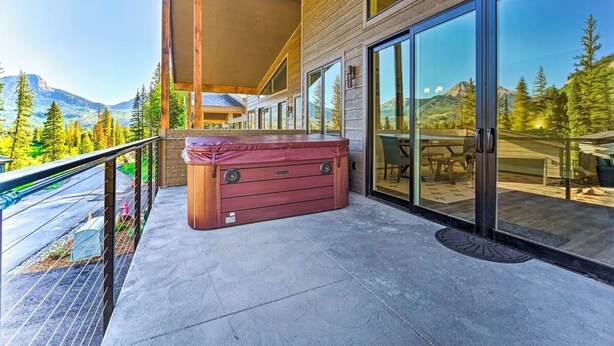 Una terrazza esterna moderna con vasca idromassaggio, ampie porte scorrevoli in vetro e vista sulle montagne.