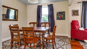 Ein Esszimmer mit Holztisch und -stühlen, einem roten Sessel und einem gemusterten Teppich.