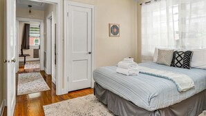 Ein Schlafzimmer mit Bett, einer Tür, einem Fenster mit Vorhängen und einem Flur, der in einen anderen Raum führt.