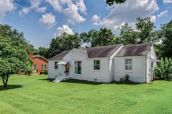 A single-story white house with a dark roof, a front porch, and a small American flag.