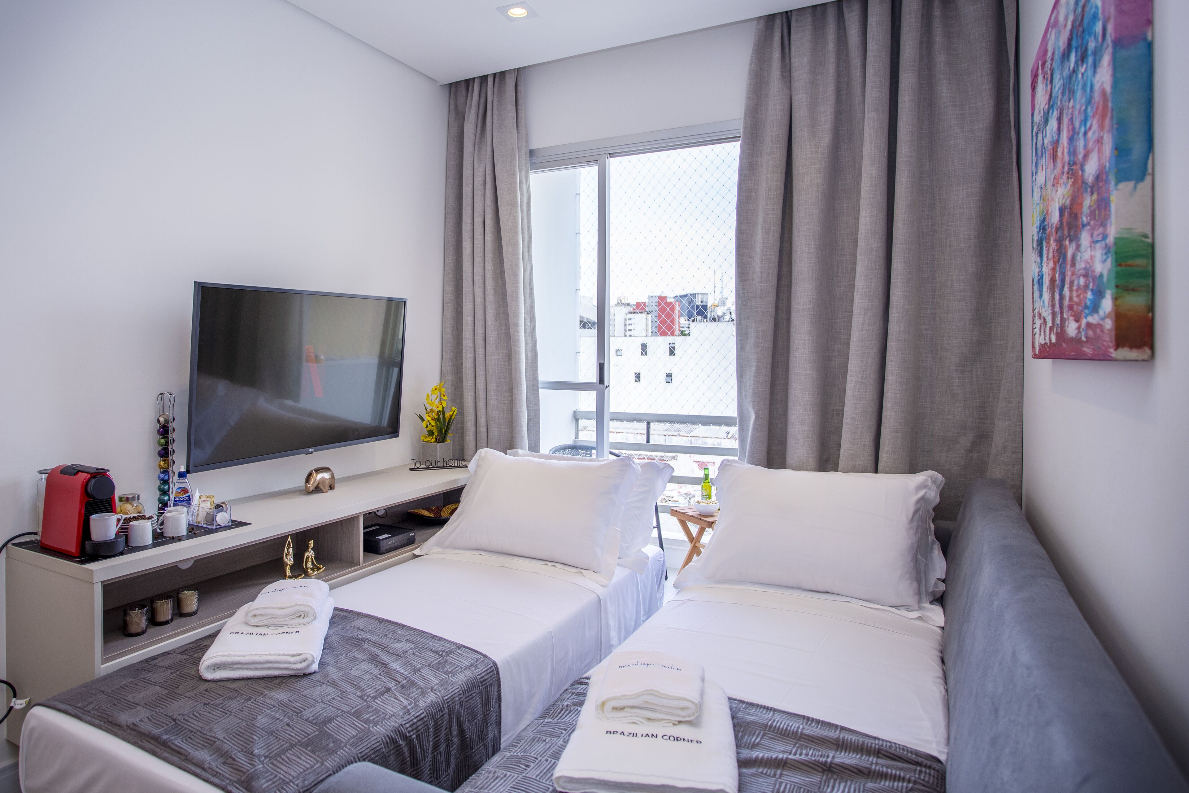 A hotel room with two beds, a TV, a coffee machine, and a window with a view of buildings.
