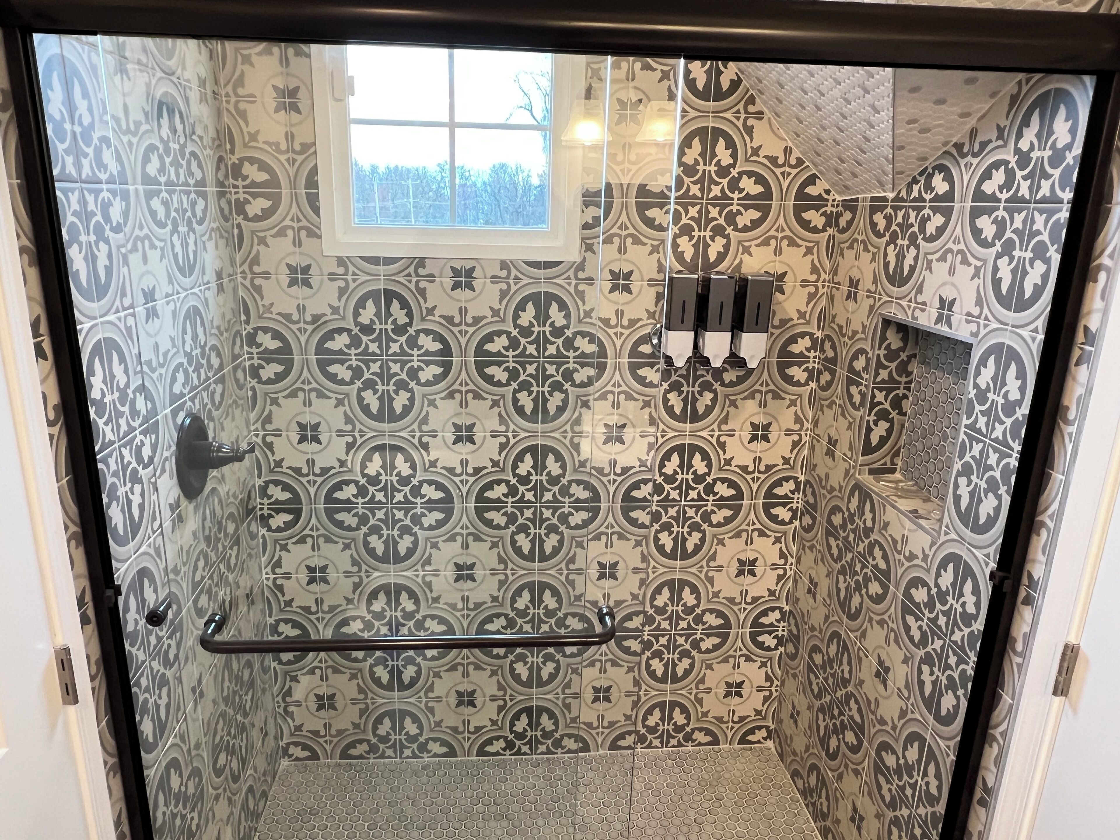 Une salle de bain avec des carreaux décorés, une fenêtre et un porte-serviettes.